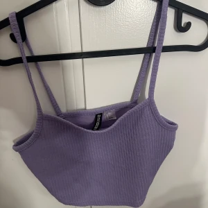 Ljuslila ribbad linnetopp H&M Divided - Superfin ljuslila ribbad linnetopp från H&M Divided. Toppen är croppad med smala axelband och har en enkel, stilren design. Perfekt att matcha med jeans eller kjol för en trendig look.
