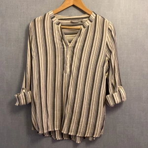 Randig henley-skjorta från Fransa - Randig henley-skjorta från Fransa i rosa blå och vitt. Skjortan har v-ringning med knappar framtill och långa ärmar som kan rullas upp och fästas med knapp. Tillverkad i mjuk bomull, perfekt för en chill och avslappnad stil.