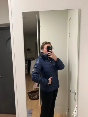 Mörkblå dunjacka från Moncler - Säljer en mörkblå dunjacka från Moncler med klassisk quiltad design och hög krage. Jackan har dragkedja framtill, fickor med dragkedja och Moncler-logga på ärmen. Se de andra bilderna för det trasiga. Det syns inte tydligt. Köpt på vintage butik i London, därmed inget kvitto och vet ej ifall äkta. Men annars super fin.