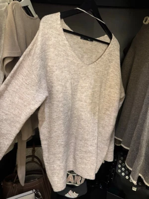 Beige stickad tröja från 157 - Mysig beige stickad tröja från 157 med v-ringning och lång ärm. Tröjan har en loose passform och är perfekt för lager på lager under höst och vinter. Enkel och stilren design som passar till allt.