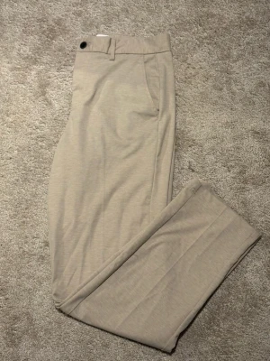 Beige chinos från Jack & Jones - Snygga beige chinos från Jack & Jones i relaxed fit. Byxorna har klassisk design med knapp och dragkedja, bälteshällor och raka ben. Perfekta för en chill och stilren look. Materialet känns mjukt och bekvämt mot huden.