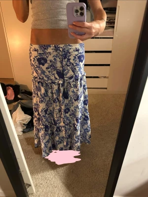 blommig långkjol från holly & whyte - supersnygg långkjol från Holly & Whyte by Lindex i vitt med blått blommönster. kjolen har volangdetaljer och resår i midjan för skön passform. perfekt till sommarens alla dagar och lätt att matcha med en enkel topp. hade svårt att göra mig av med denna fina kjol men började bli för liten i midjan tyvärr🥹