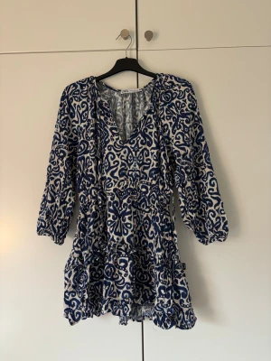 Blåvit kortklänning från Zara - Säljer en blåvit kortklänning från Zara med unikt mönster och v-ringad hals. Klänningen har trekvartsärmar och volangdetaljer nedtill. 💙