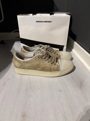 Beige mockasneakers från Lanvin - Säljer ett par stilrena sneakers från Lanvin i beige mocka med vita gummidetaljer och rund tå. Skorna har beige snörning och vit sula med diskret logga undertill. Perfekta för dig som gillar minimalistisk och clean stil. Toe box och sulor är i bra skick men mockan är sådär med lite rengöring blir den säker bättre därför billigt pris och priset är inte fast 