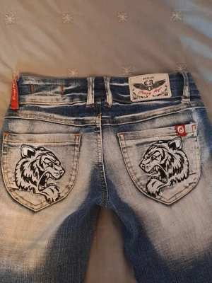 Crazy age jeans med tigertryck - Säljer ett par jeans från Crazy Age med coolt tigertryck på fickorna. Jeansen har låg midja, bootcut-modell och har många snygga detaljer. Säljer då de tyvärr är för små för mig i midjan, annars är de i princip helt nya. Förhandlingsbart pris, skriv gärna om du har några frågor eller vill ha fler bilder :) 