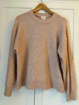 Beige stickad tröja med paljetter H&M - Mysig ljusrosa stickad tröja från H&M i storlek S. Tröjan har ett glittrigt paljettmönster över hela och ribbade muddar vid ärmslut och nederkant. Perfekt för dig som gillar lite extra bling i vardagen.