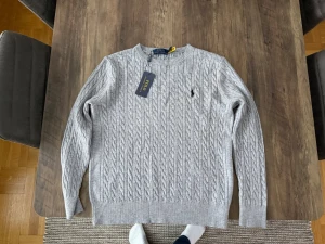 Grå kabelstickad tröja Polo Ralph Lauren - Säljer en grå kabelstickad tröja från Polo Ralph Lauren i storlek S. Tröjan har rund hals, lång ärm och den klassiska broderade loggan på bröstet. Tillverkad i mjuk bomull och har ribbade muddar vid ärmslut och nederkant. Perfekt för lager på lager under höst och vinter.