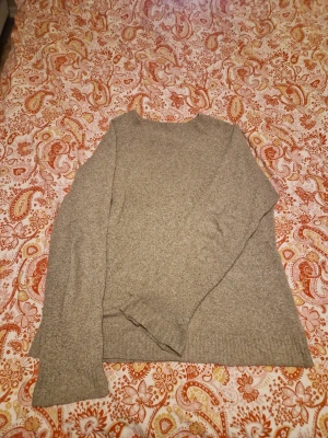 Beige stickad tröja från Vero Moda - Mysig beige stickad tröja från Vero Moda i storlek S. Tröjan har en klassisk rund halsringning, långa ärmar och ribbade muddar vid ärmslut och nederkant. Perfekt för lager-på-lager under kyliga dagar.