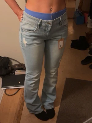 Ljusblå bootcut jeans från H&M - Säljer ett par ljusblå jeans från sellpy med bootcut-modell. Jeansen har slitna detaljer framtill och bak, klassiska fem fickor och en snygg tvätt. Materialet är mjukt jeans och passformen är normal med låg midja. Som ni ser på sista bilden är de för stora i midjan och säljer därför. Storleken står 31/32 och passar mig i längd 164.