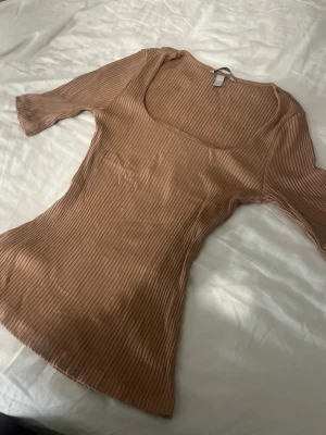 Beige ribbad topp med fyrkantig ringning - Säljer en beige ribbad topp med trekvartsärm och snygg fyrkantig ringning. Toppen är figurnära men stretchig. De är tjockare tyg med extra tyg på insidan. Använt 1 gång. 