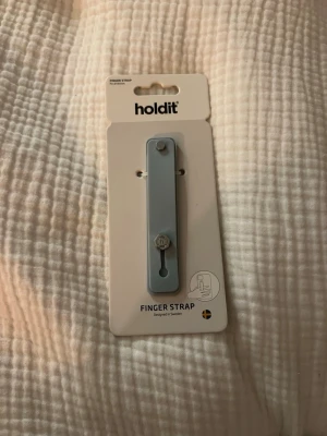Finger strap från Holdit - En helt oanvänd finger strap holder från Holdit i ljusblå färg. Köpte den och ångrade mig!