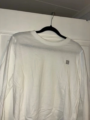 Vit långärmad tröja från Calvin Klein - Vit långärmad tröja från Calvin Klein med rund halsringning och diskret CK-logga på bröstet. Tröjan är i mjuk bomull och har en clean, enkel look som passar till allt. Perfekt för dig som gillar stilrena basics.
