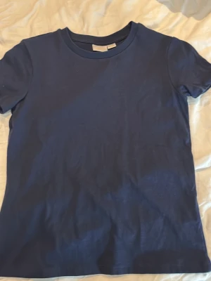 Mörkblå basic t-shirt - En enkel och stilren mörkblå t-shirt med rund hals och korta ärmar. Perfekt att matcha med jeans eller shorts för en clean look. Tillverkad i mjuk bomull som känns skön mot huden.