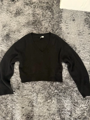 Svart stickad tröja  - Svart stickad tröja med v-ringad hals och bred ribbad kant nedtill. Tröjan har lång ärm och är perfekt för lager på lager under höst och vinter. Enkel och stilren design som passar till allt.