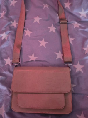 Beige axelväska i crocopräglat skinn - Snygg beige axelväska med crocopräglat mönster och justerbar bred axelrem. Väskan har ett stilrent och modernt utseende med flera fack inuti för bra organisering. Perfekt för dig som vill ha en trend sopren look och ändå få plats med det viktigaste.