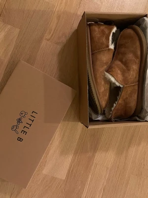 Bruna inomhustofflor från Little B med foder - Säljer ett par snygga bruna inomhustofflor från Little B med mjukt vitt foder på insidan. Tofflorna är i fint skick, original box och paper finns. Enda skadan är att flärpen har gått av på högra skon. (Syns på bild 4 ) Nypris ca 650 kr mitt pris endast 150 kr. Fraktar inom 1 dag, om du har någon fundering så är det bara att höra av sig😊
