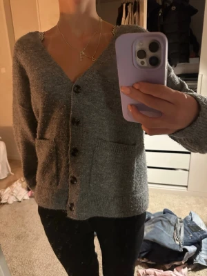 grå kofta från Gina Tricot - mysig grå kofta från Gina Tricot med v-ringning och stora knappar framtill. koftan har två fickor och är stickad i mjukt material, perfekt för lager på lager under kyliga dagar. passar till allt och har en klassisk, enkel look som man kan styla enkelt till ett par kostym byxor eller ett par jeans. alltid där när outfiten känns tråkig eller när sommardagen känns kall💞