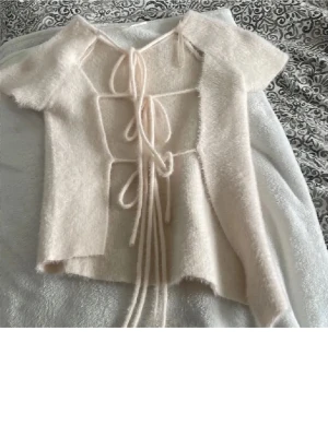 Beige stickad topp med snörning - Supersöt beige stickad topp med korta ärmar och snygg snörning framtill. Mjuk och fluffig känsla, perfekt för dig som vill ha något unikt och trendigt. Passar till både jeans och kjol för en chill look.