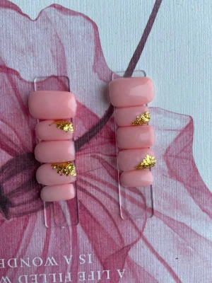 Rosa lösnaglar med gulddetaljer - Snygga lösnaglar i en mjuk rosa nyans med skimrande guldfolie som accent. Naglarna har en kort, fyrkantig form och en glansig finish. Perfekt för dig som vill ha en elegant och trendig look utan att behöva gå till salong.