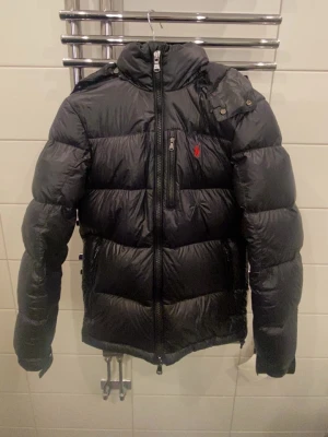 jacka Ralph Lauren - Säljer en svart pufferjacka från Polo Ralph Lauren i storlek XS. Jackan har en klassisk röd broderad logga på bröstet, huva och flera dragkedjeförsedda fickor. Tillverkad i glansig polyester och perfekt för kalla dagar. Priset kan diskuteras 