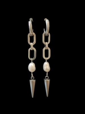 Silvriga örhängen med sötvattenspärlor och konformad avslutning -  Unika örhängen i modern design med kedjelänkar, äkta sötvattenspärlor och en elegant konformad detalj.   Finns även i guldpläterad variant.  Priset avser ett par örhängen  Material: Rostfritt stål  & sötvattenspärlor Längd: ca 6,5 cm Nickelfria och handgjorda