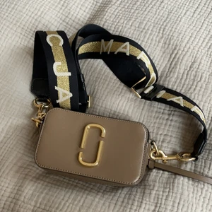 Marc Jacobs Snapshot - Marc jacobs populära snapshot small camera bag. Färgena beige, svart och cremevit med guldiga detaljer. Bandet går att byta ut och mixa med andra färger. Bandet är guldigt/vitt/svart med guldiga detaljer. Även väskan har guldiga detaljer. Jättefint skick då den knappt är använd! Nypris ca 3400kr. 