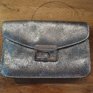 Superfin Marc by Marc Jacobs festväska - Säljer min fina gamla partyväska i silvrigt skinn från Marc by Marc Jacobs. Inköpt 2011 tror jag. Den är i superfint skick. Axelremmen som hörde till är borta. Kan inte hitta några direkta skavanker mer än att spännet är lite nött. Finns plats för kort i så man behöver inte ta med plånboken. Såklart äkta.