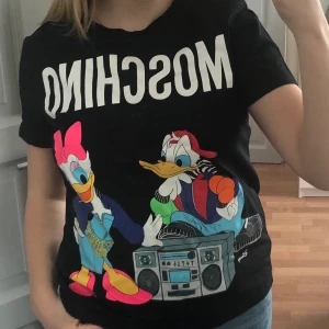 Moschino t-shirt - Moschino t-shirt med tryck. Aldrig använd. Passar för S/M. Skriv vid intresse. Fraktkostnad tillkommer, kan dock mötas upp i Stockholm :) 