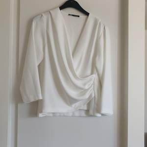 En vit blus med rynkad omlott detalj fram från Zara i storlek M. Materialet är 100% polyester. Fraktkostnaden tillkommer.