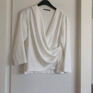 Vit blus Zara stl M - En vit blus med rynkad omlott detalj fram från Zara i storlek M. Materialet är 100% polyester. Fraktkostnaden tillkommer.