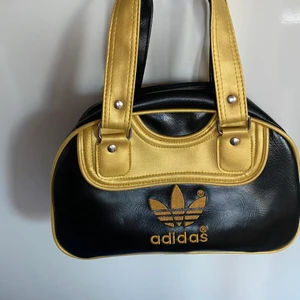 Adidasväska guldig och svart - Jag säljer min ADIDAS väska som såklart är äkta. Säljer pga att det inte är min stil längre, men den har häller inga större defekter. Den är rymlig med ett stort och ett litet fack. Skriv vid intresse!💗