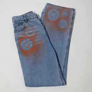 Högmidjade jeans i rak och lös fit. Oranga detaljer i ”smiley”motiv på byxbenet och vid fickan. Ursprungligen H&M jeans som är omgjorda av Scannable UF. Genom att skanna en QR-kod som finns fäst på plagget kan du läsa mer om materialet och dess miljöpåverkan!