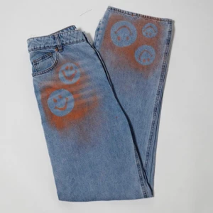 Smiley jeans - Högmidjade jeans i rak och lös fit. Oranga detaljer i ”smiley”motiv på byxbenet och vid fickan. Ursprungligen H&M jeans som är omgjorda av Scannable UF. Genom att skanna en QR-kod som finns fäst på plagget kan du läsa mer om materialet och dess miljöpåverkan!