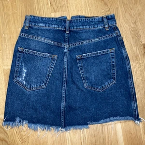 mörkblå kjol, storlek 34 - En mörkblå kjol med en liten dragkedja vid magen samt en knapp. Sliten nere vid kjolen, lite på baksidan men även lite på fickorna på framsidan vilket är själva modellen på kjolen som är snyggt. Använd Ca 1/2 gånger länge sedan. 2/3 år gammal. 