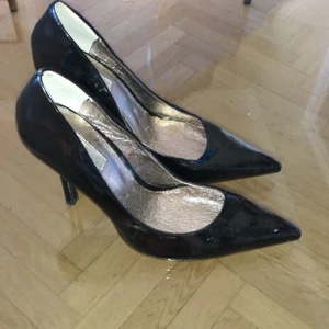 Donna Girl stilettklackar  - Oanvända stilettklackar från Donna Girl säljes. Svart lack i imitationsläder. Klackhöjd 10 cm.  
