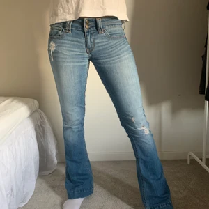 lågmidjade utsvängda jeans  - Jag säljer dessa super snygga jeansen ifrån hollister. De är blå med slitningar och har två knappar. Dem är köpta för 1000kr och säljs nu för 299kr. Priset kan diskuteras. Storleken är 25w vilket motsvarar xs. Köparen står för frakt♥️  