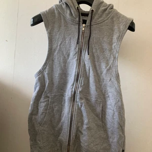 kofta - En grå sleeveless kofta med fickor och luva, med silvriga och svarta detaljer