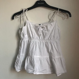 Söt sommrig topp - Säljer denna väldigt söta toppen som jag inte använder nog mycket. Den har små rosetter på ärmarna och där framme som man knyter själv efter önskad längd.