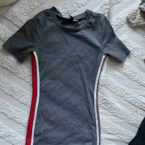 Tajt grå klänning - Tajt grå klänning med röda och vita linjer. Storlek 40.