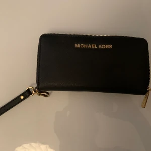 Michael Kors Plånbok  - Michael Kors plånbok, kan användas som liten väska då den har ett ”armband” 10x18cm. Skickar gärna med postens skicka lätt som är spårbart. Inköpt på Jackie 2020. 