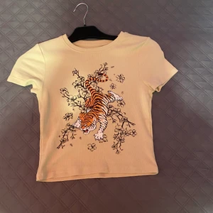 Beige ”tiger tröja” från new yorker strl xxs/xs/m - En beige croppad(inte jättekort) t-shirt. Jag har bara använt tröjan två gånger och jag säljer den för att jag inte gillar den längre. Tröjan är väldigt stretchig & passar därför fletal strl! Persoblogen så stylade jag dne bara med ett par baggy byxor och lite smycken💗