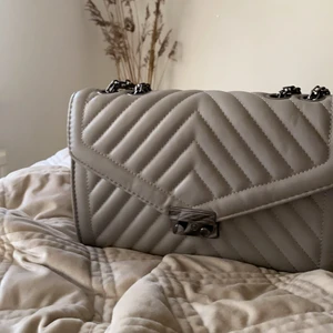 Grå handväska  - Super snygg väska som tyvär aldrig kommer till användning. Är i grått skinn med silver detaljer. Aldrig använd och är som i ny skick. 