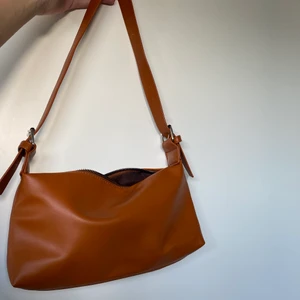 Axelväska brun/orange - Axelväska i en varm brun färg. Aldrig använd! Bredd: 28 cm. Höjd: 14 cm. Köparen står för frakt