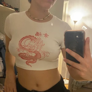 croppad top med röd drake på - En vit ribbad croppad topp med tryck på en röd drake. Så bekväm, dock inte min stil längre! Sitter bra på mig som har strl M i vanliga fall, funkar nog på en s eller en l med mindre byst. 