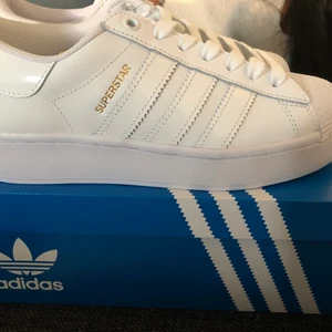 Adidas sneakers  - Ett par vita adidas sneakers med guld detaljer och glansiga stripes på sidorna. Använd 2 gånger, inprincip nya. Strl 39 1/3 - säljer pga för stor storlek. 
