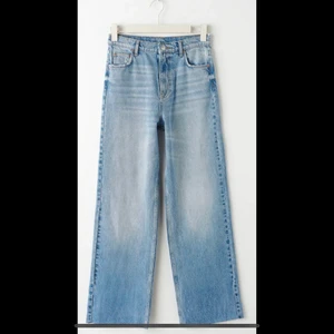 Ginatricot jeans  - Petite jeans med superhög midja. Jeansen är blåa och utan stretch och har raka, vida byxben med fullängd. De har dragkedjegylf och rå kan vid bensluten. 