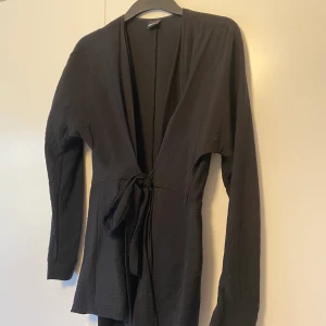 Blus - Svart blus med knytning i midjan. I strl 34.