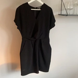 Svart klänning - Svart omlottklänning från Primark. Klänningen går omlott över bröstet och är figurformad med två fickor på vardera sida. Dragkedja i ryggen. Oanvänd! Storlek 42