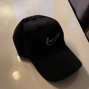 Nike keps svart onesize - Supersnygg och cool keps från Nike i färgen svart. Nikemärket på kepsen är svart med vita konturer, och kepsen går att dra åt eller spänna av där bak. Använd endast en gång, så den är i mycket bra skick! Frakt tillkommer. 