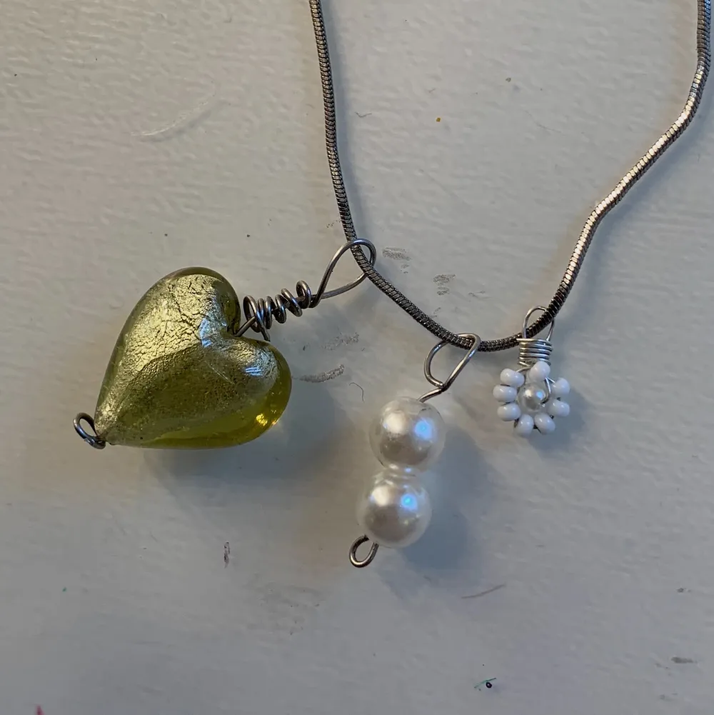 Silverkedja med ett grönt glashjärta, en liten vit blomma och två vita pärlor💚✨. Accessoarer.